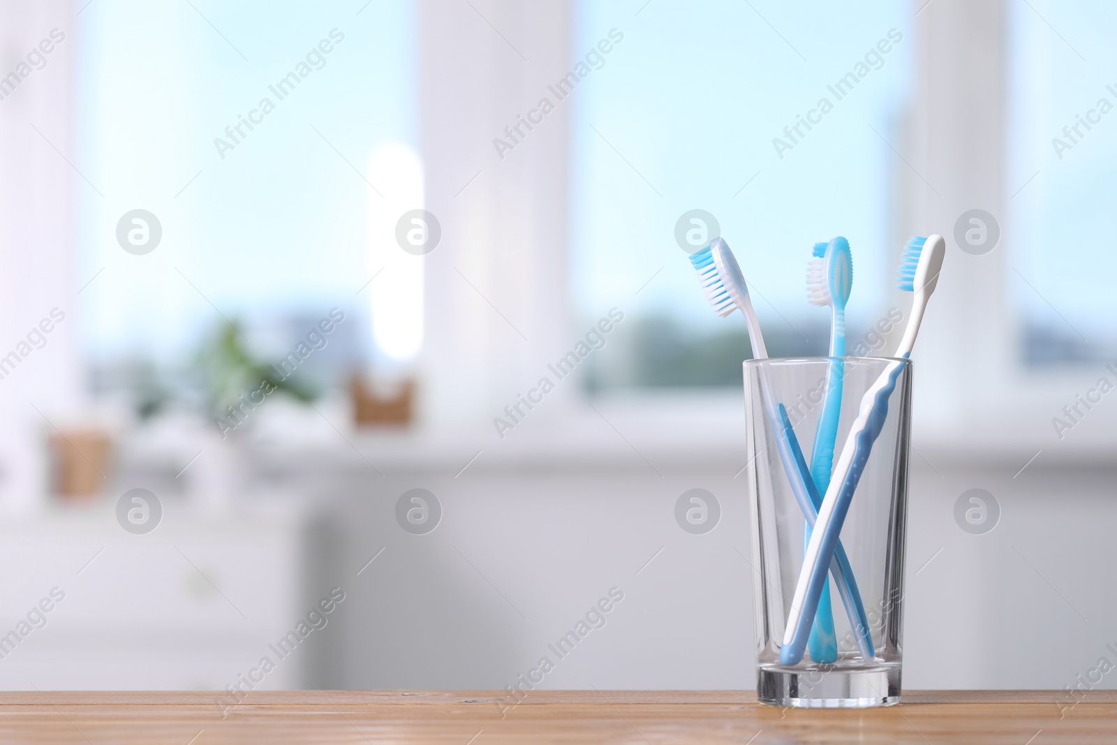 Photo of Plastic toothbrushes in holder on wooden table indoors. Space for text