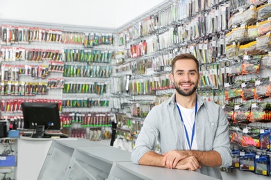 Photo of Salesman standing near showcase with fishing equipment in sports shop. Space for text