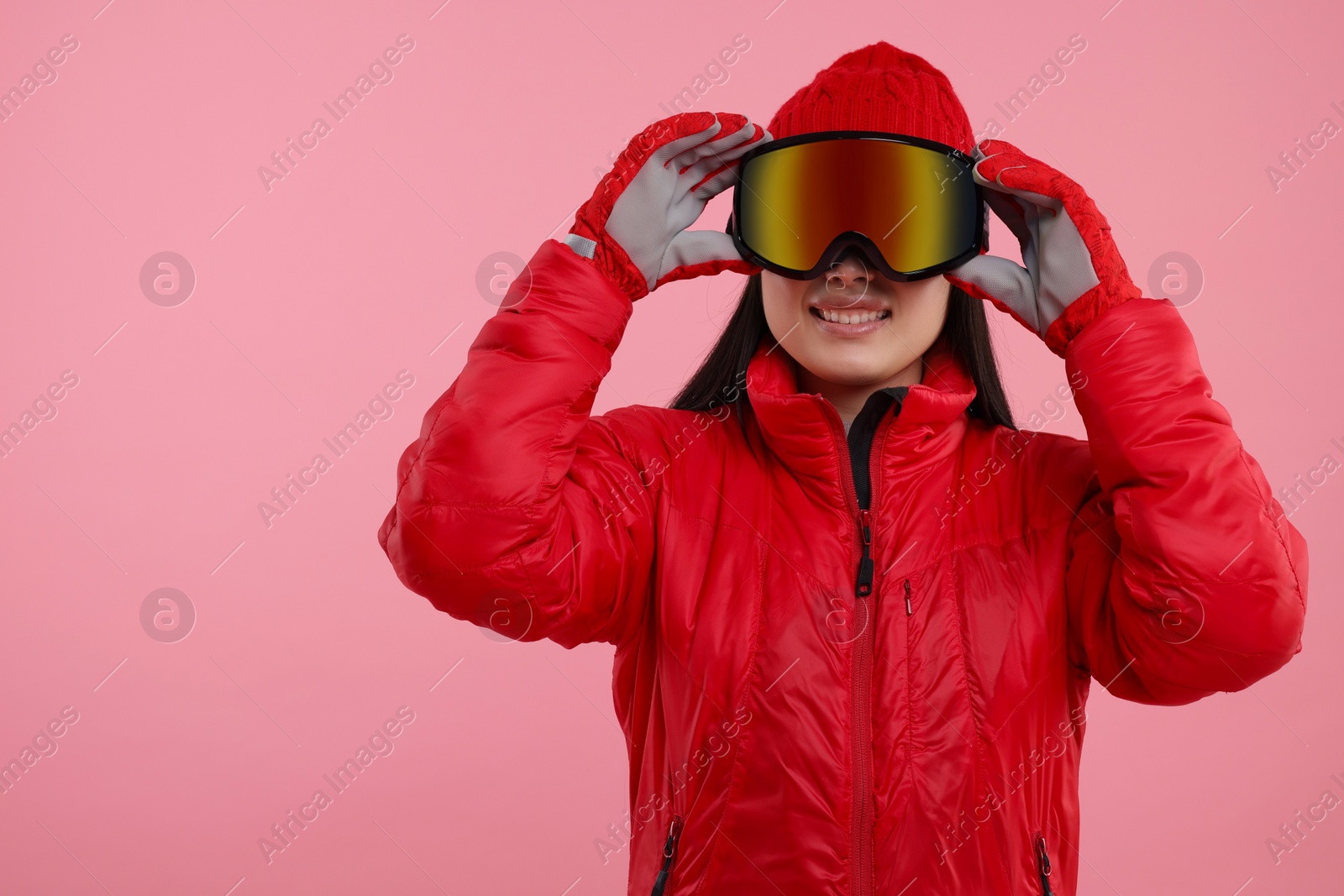 Photo of Happy woman in winter sportswear and goggles on pink background. Space for text