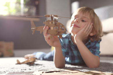 Little boy playing with cardboard helicopter on floor at home. Creative hobby