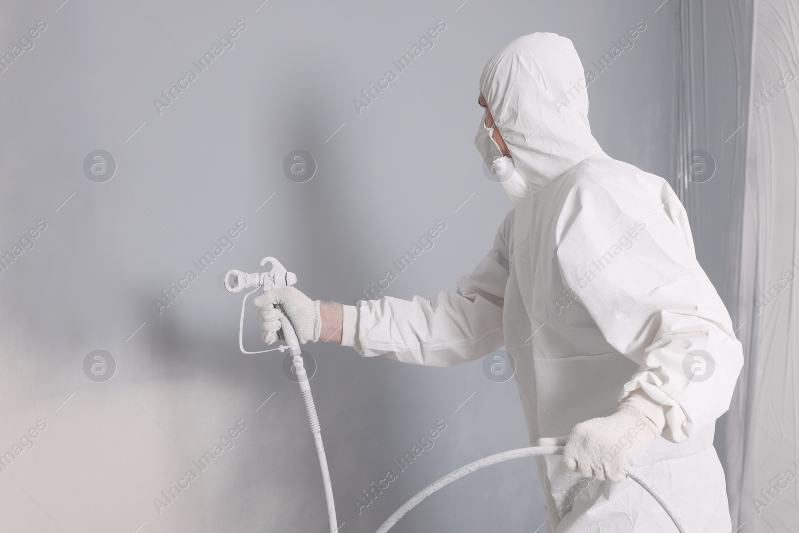 Photo of Decorator dyeing wall in grey color with spray paint