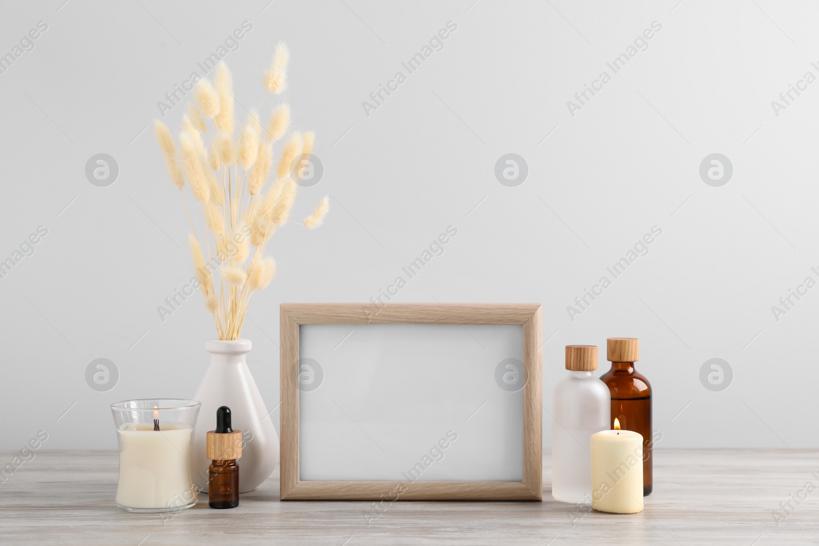 Photo of Blank photo frame, different bottles and decor elements on wooden table