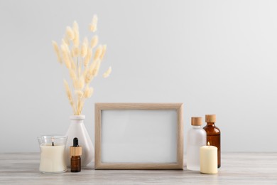 Photo of Blank photo frame, different bottles and decor elements on wooden table
