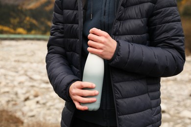 Photo of Boy holding thermo bottle with drink in mountains, closeup