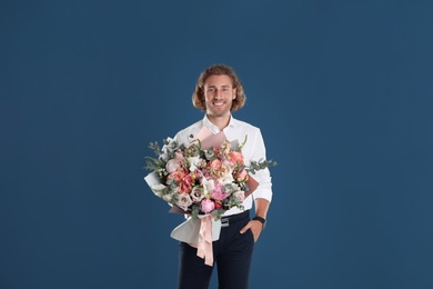 Photo of Young handsome man with beautiful flower bouquet on blue background