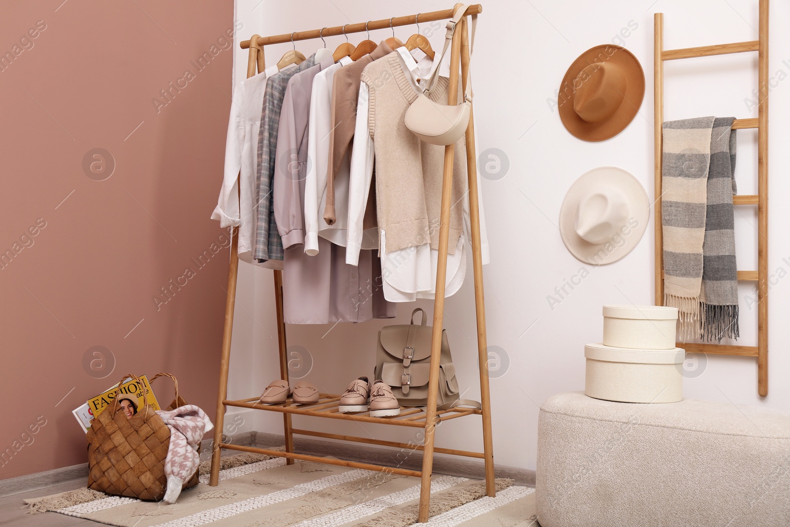 Photo of Rack with different stylish clothes and shoes near white wall in room