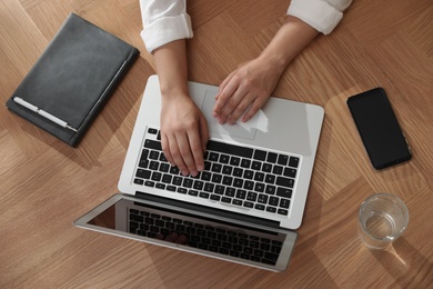 Photo of Young woman using laptop for search at wooden table, top view