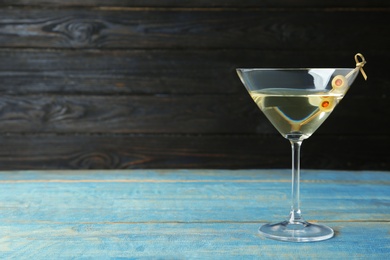 Photo of Glass of Classic Dry Martini with olives on light blue wooden table against dark background. Space for text