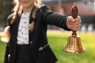 Photo of Closeup view of pupil holding school bell outdoors on sunny day