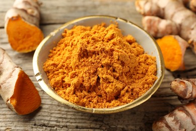 Photo of Aromatic turmeric powder and raw roots on wooden table, closeup