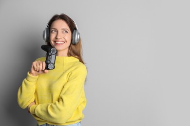 Happy woman in headphones with game controller on light grey background. Space for text