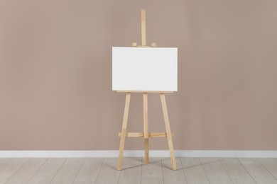 Photo of Wooden easel with blank canvas near beige wall