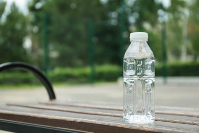 Bottle with water on wooden bench outdoors. Space for text