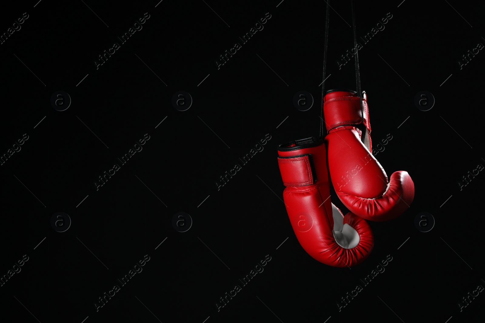 Photo of Pair of red boxing gloves hanging on black background, space for text