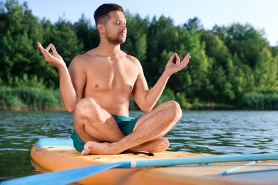 Man meditating on color SUP board on river