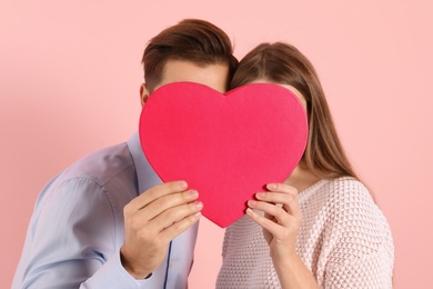 Man and woman hiding behind decorative heart on color background. Valentine's day