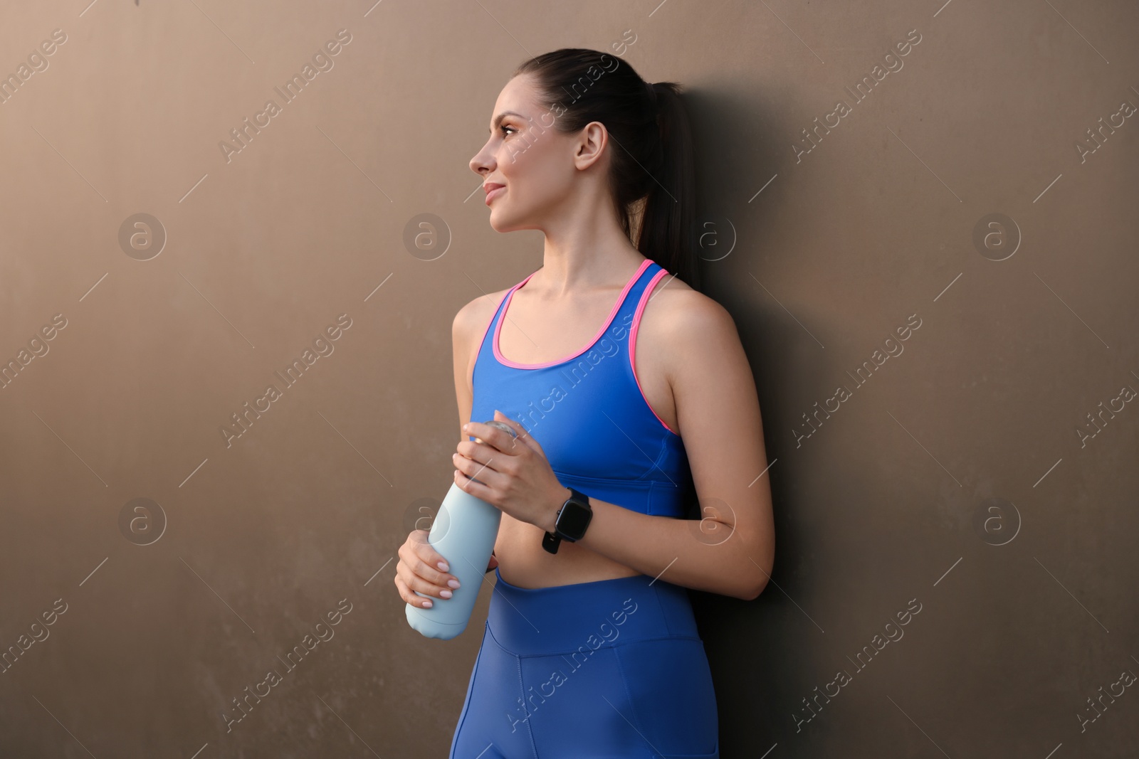 Photo of Beautiful woman in stylish sportswear with bottle of drink near black wall