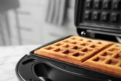 Photo of Modern iron with tasty Belgian waffles on table, closeup