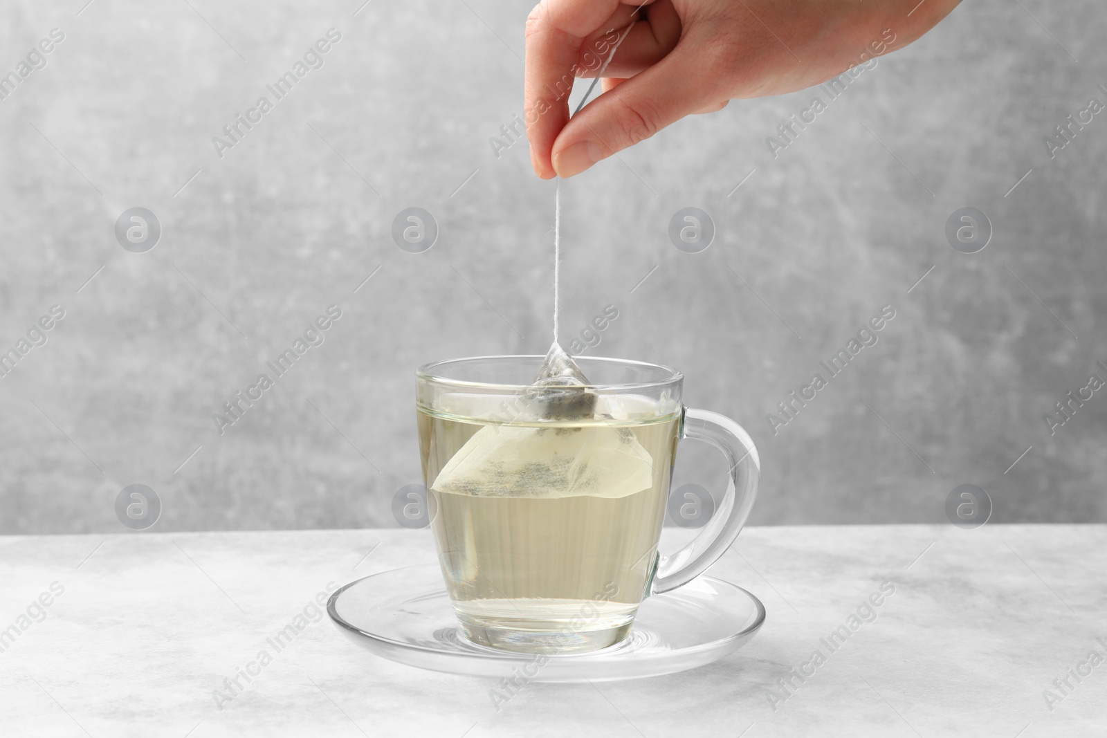 Photo of Tea brewing. Woman putting tea bag into cup at light table, closeup