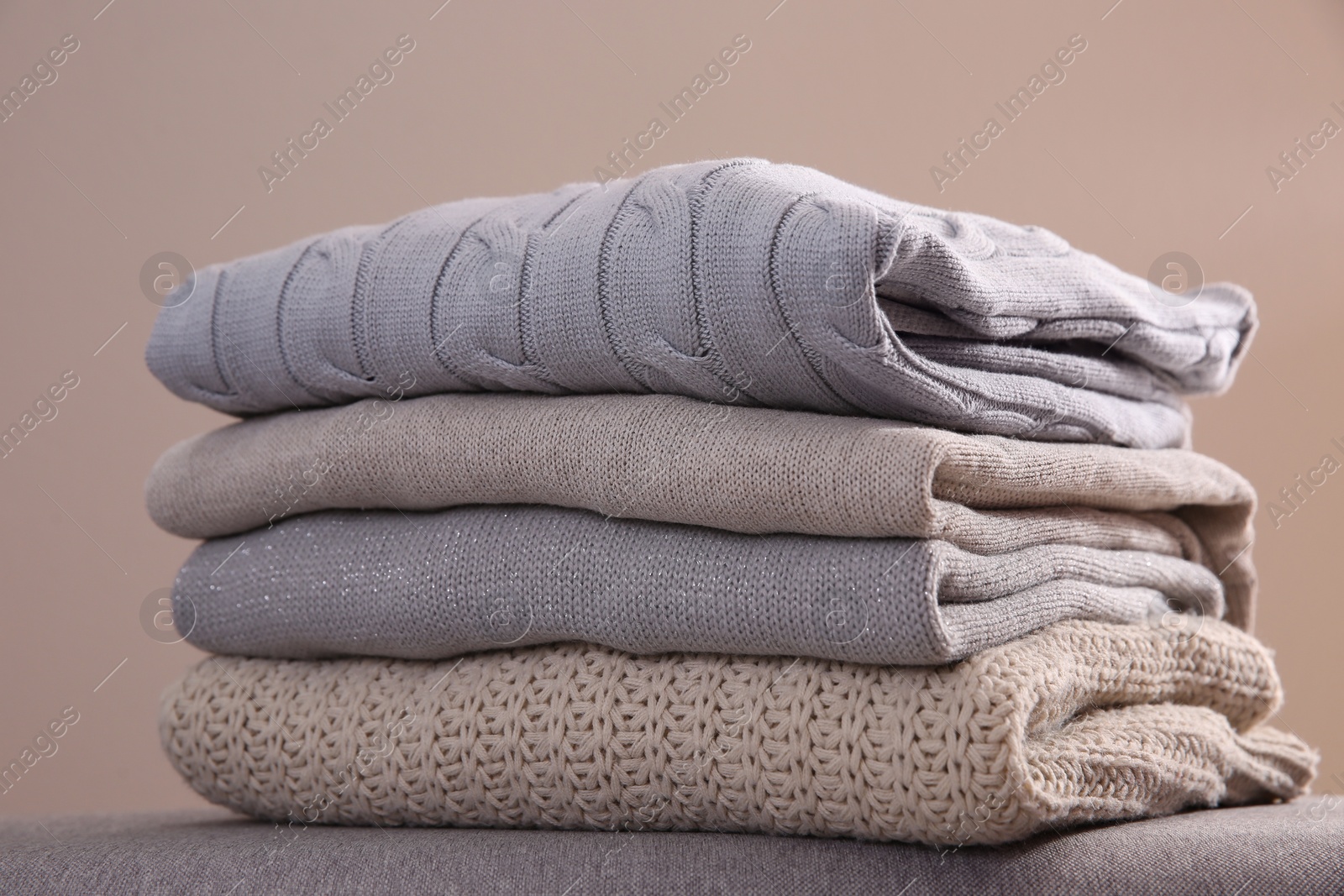 Photo of Stack of folded warm sweaters against grey background, closeup
