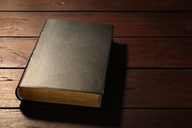 Old hardcover Bible on wooden table, space for text. Religious book