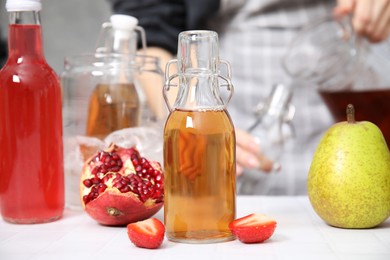 Photo of Making kombucha. Woman pouring drink from jug into bottle indoors, selective focus