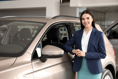 Young saleswoman near new car in dealership