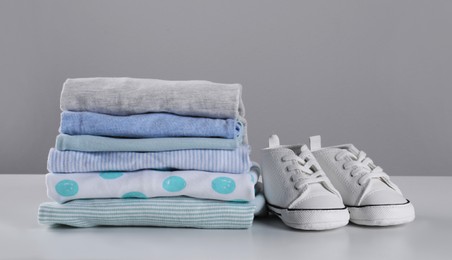 Stack of clean baby's clothes and small shoes on table against light grey background