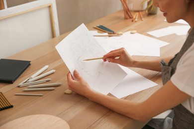 Photo of Young woman drawing male portrait at table indoors, closeup