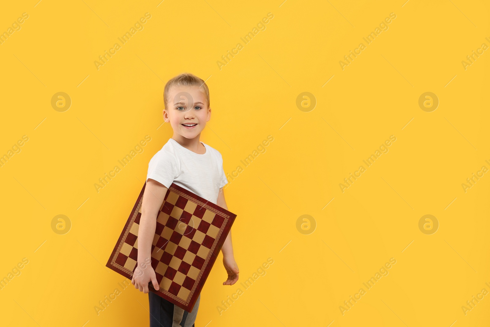 Photo of Cute girl holding chessboard on orange background. Space for text