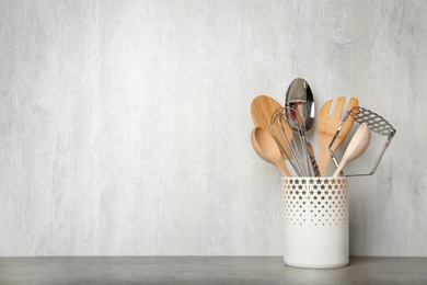 Photo of Holder with kitchen utensils on grey table against light background. Space for text