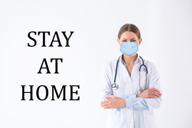 Young doctor in medical mask and text STAY AT HOME on white background