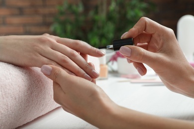 Photo of Manicurist applying polish on client's nails at table, closeup. Spa treatment