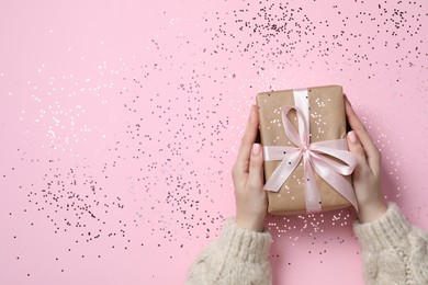 Christmas present. Woman holding gift box and confetti on pink background, top view. Space for text