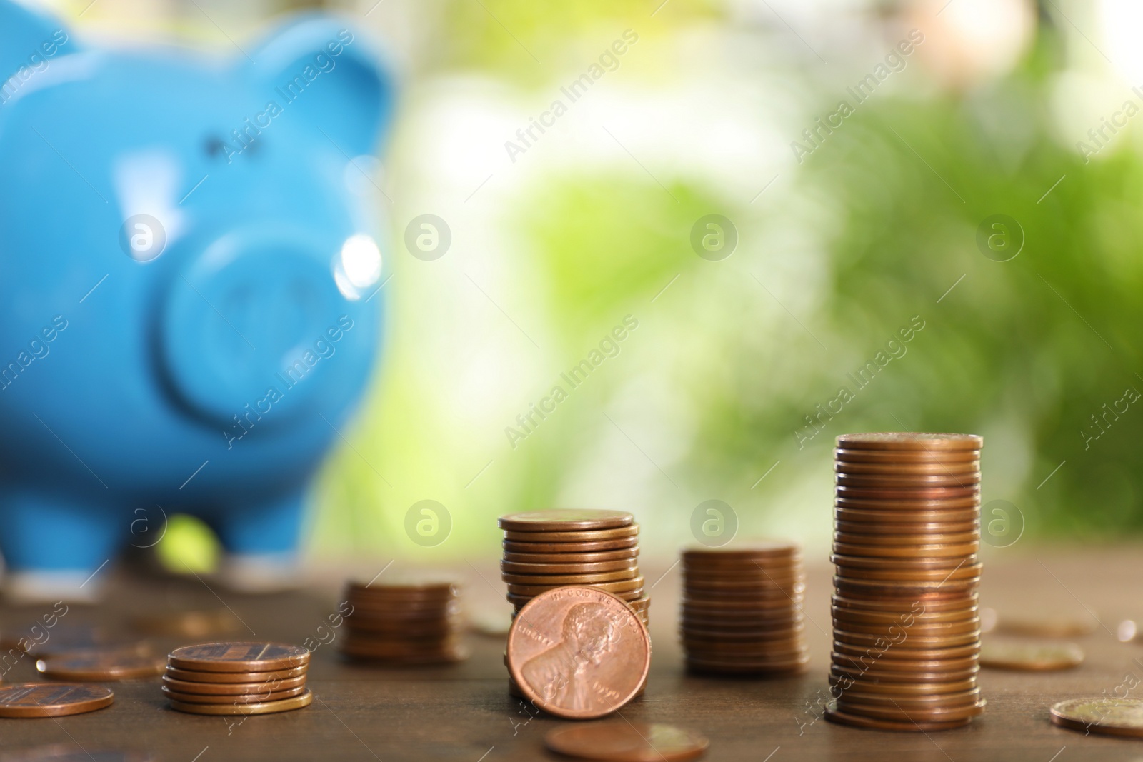 Photo of Many metal coins and piggy bank on wooden table against blurred green background. Space for text