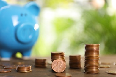 Many metal coins and piggy bank on wooden table against blurred green background. Space for text