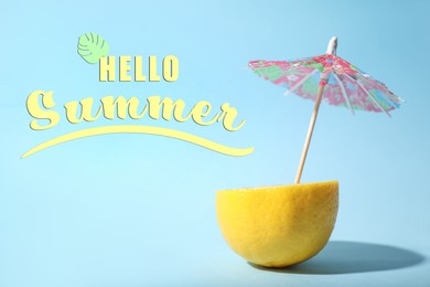 Hello Summer. Creative image of summer cocktail made with lemon and small paper umbrella on light blue background,