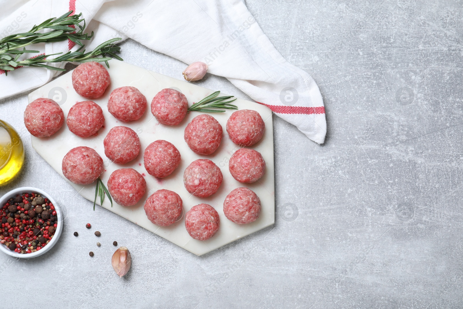 Photo of Many fresh raw meatballs and ingredients on light grey table, flat lay. Space for text