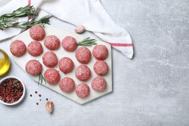 Many fresh raw meatballs and ingredients on light grey table, flat lay. Space for text