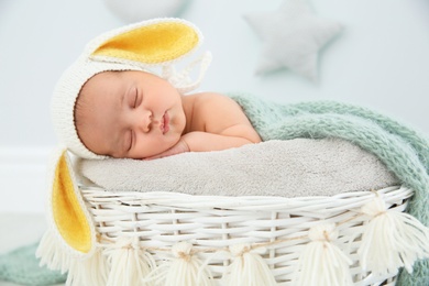 Photo of Adorable newborn child wearing bunny ears hat in baby nest indoors