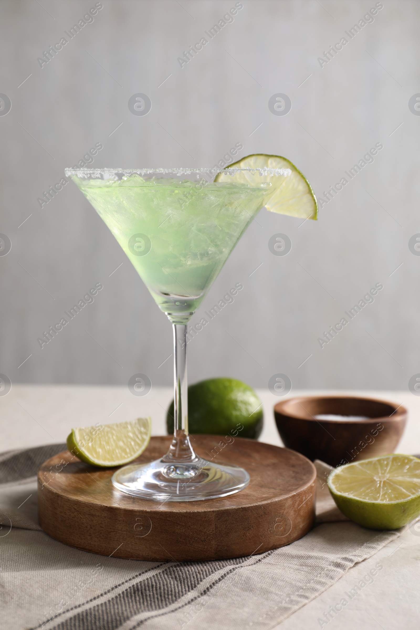 Photo of Delicious Margarita cocktail in glass, salt and limes on table