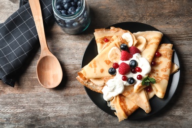 Thin pancakes with berries and cream on plate, top view