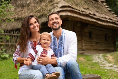 Photo of Happy family in Ukrainian national clothes sitting on bench outdoors