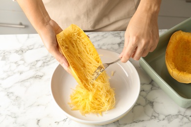 Photo of Woman scraping flesh of cooked spaghetti squash with fork in kitchen