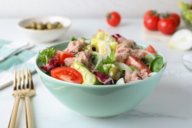 Photo of Bowl of delicious salad with canned tuna and vegetables served on white marble table