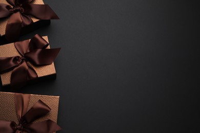 Photo of Brown gift boxes decorated with satin bows on black background, flat lay. Space for text