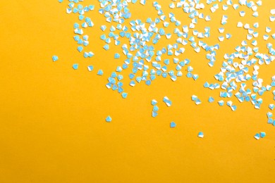Photo of Shiny bright light blue glitter on yellow background, flat lay. Space for text