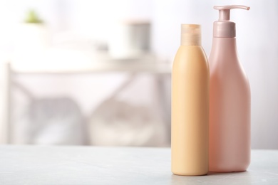 Bottles with hair care cosmetics on table in bathroom, space for text