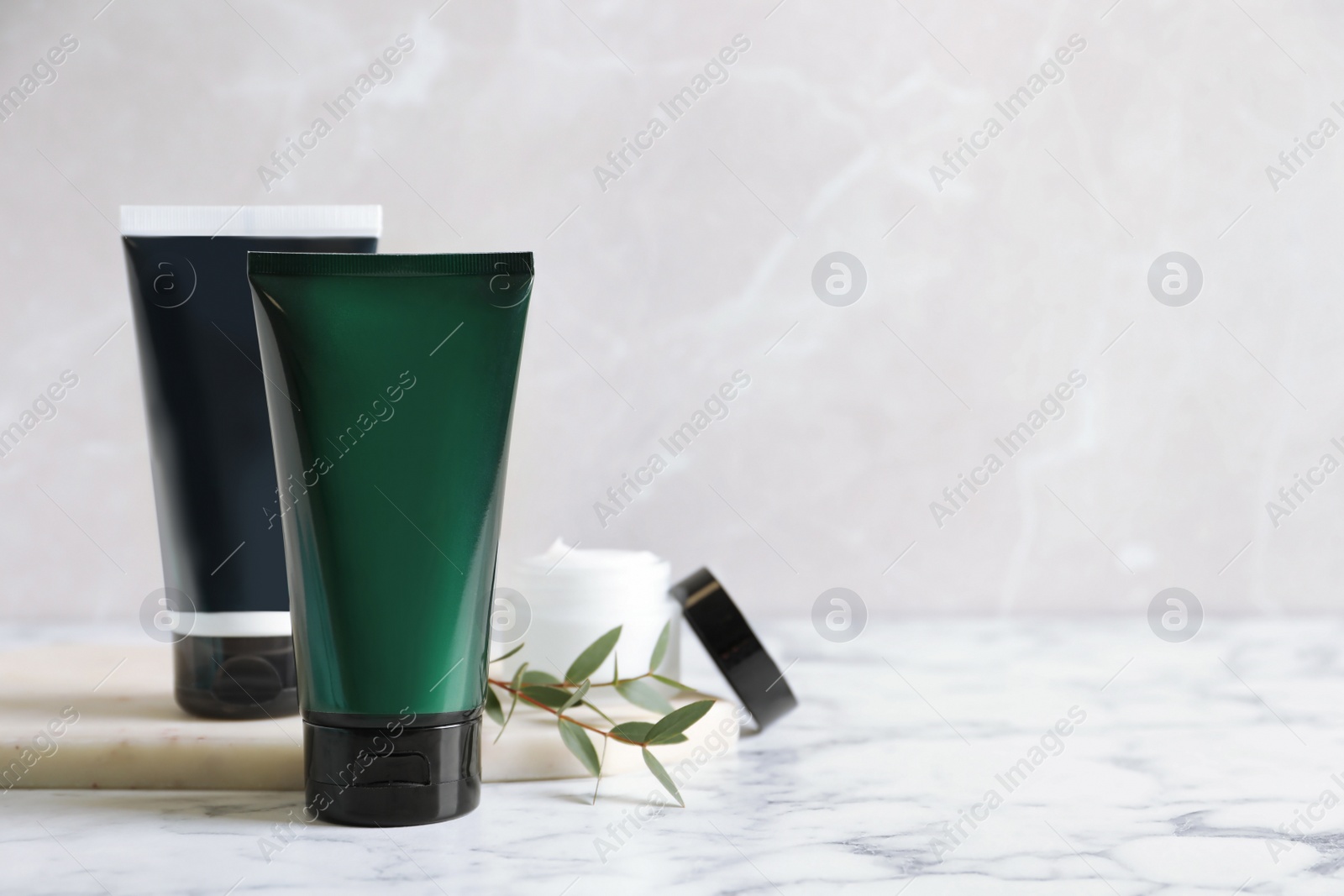 Photo of Tubes and jar of men's facial cream on white marble table. Space for text