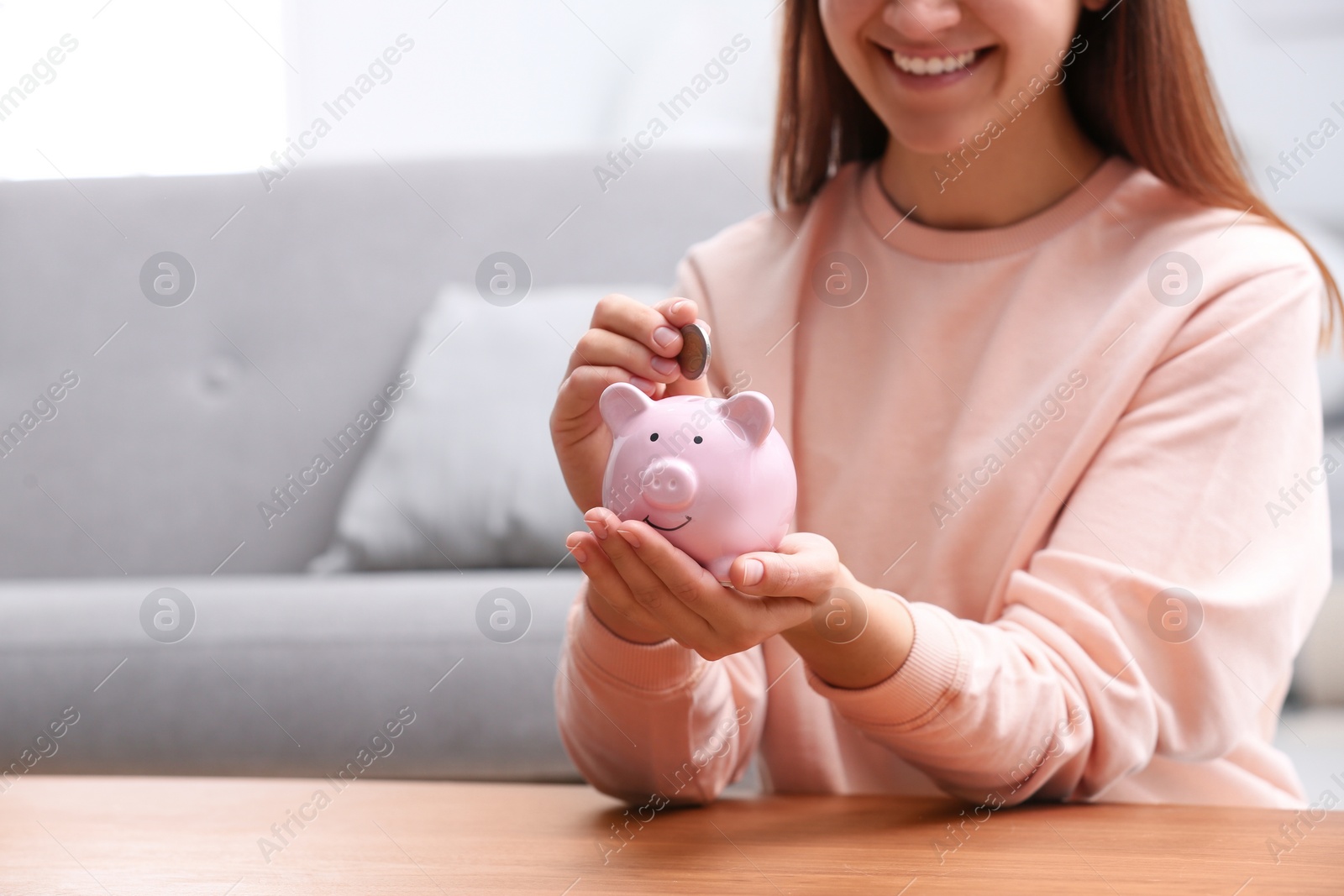 Photo of Woman putting coin into piggy bank at wooden table, closeup